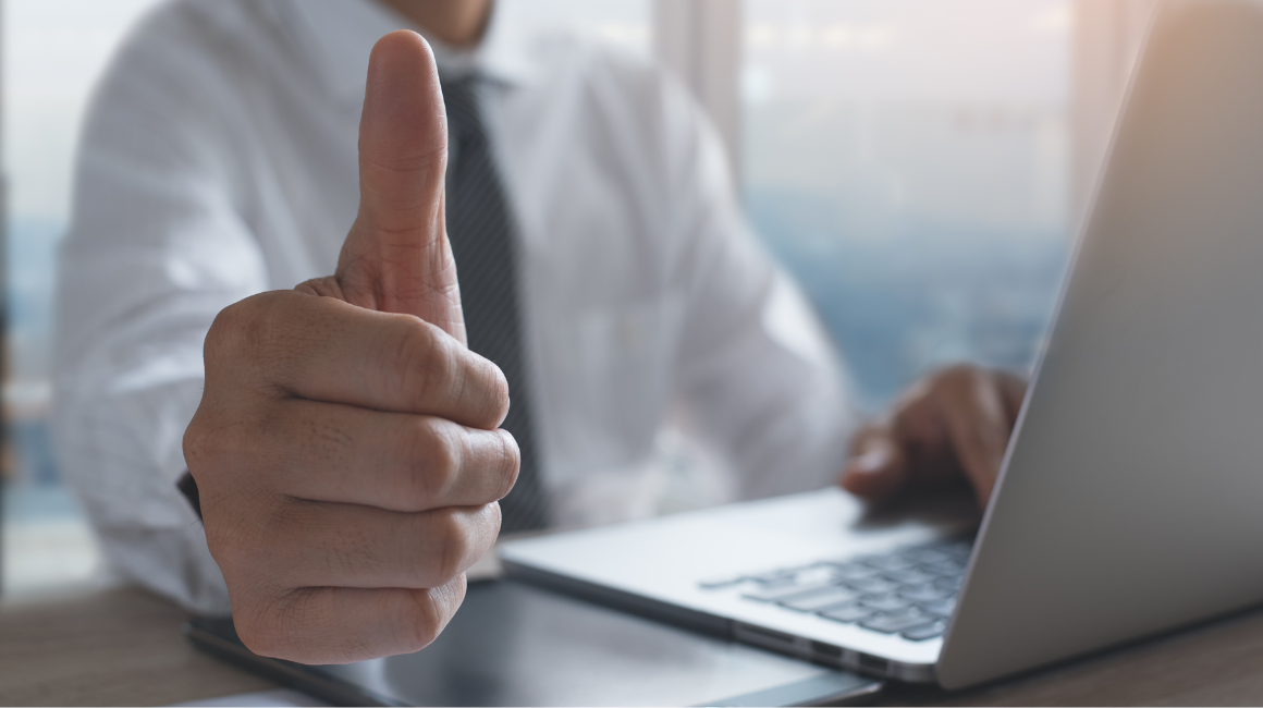 Mężczyzna w biurze pokazujący kciuk w górę przed laptopem